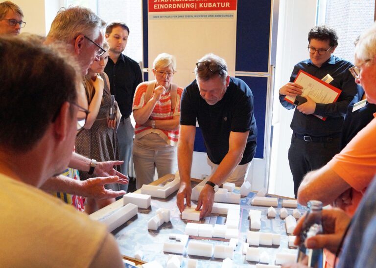 Eine Gruppe von Menschen diskutiert um ein Architekturmodell in einer Präsentation.