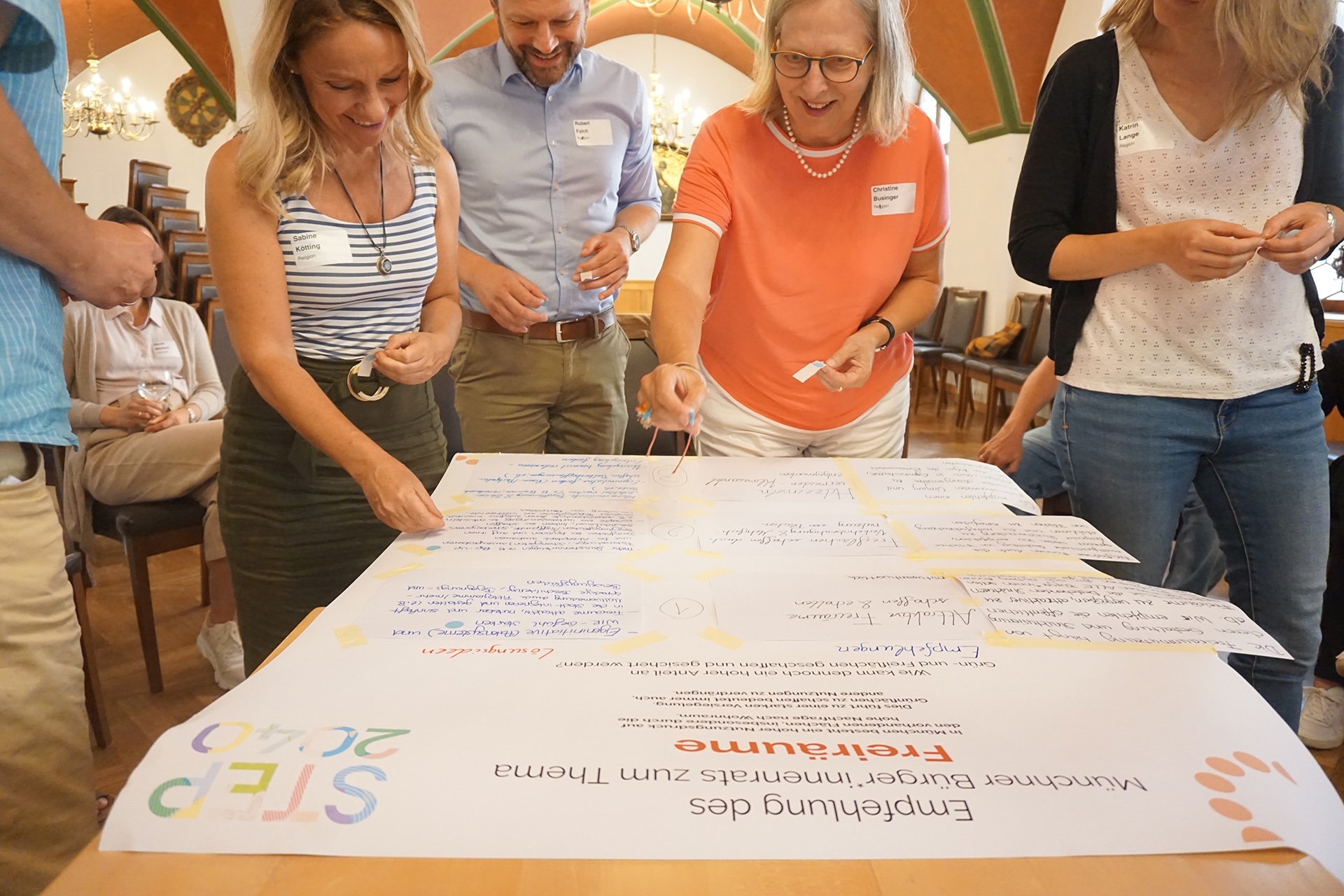 Gruppendiskussion mit mehreren Personen, die an einem gro&szlig;en Plakat mit Notizen arbeiten.