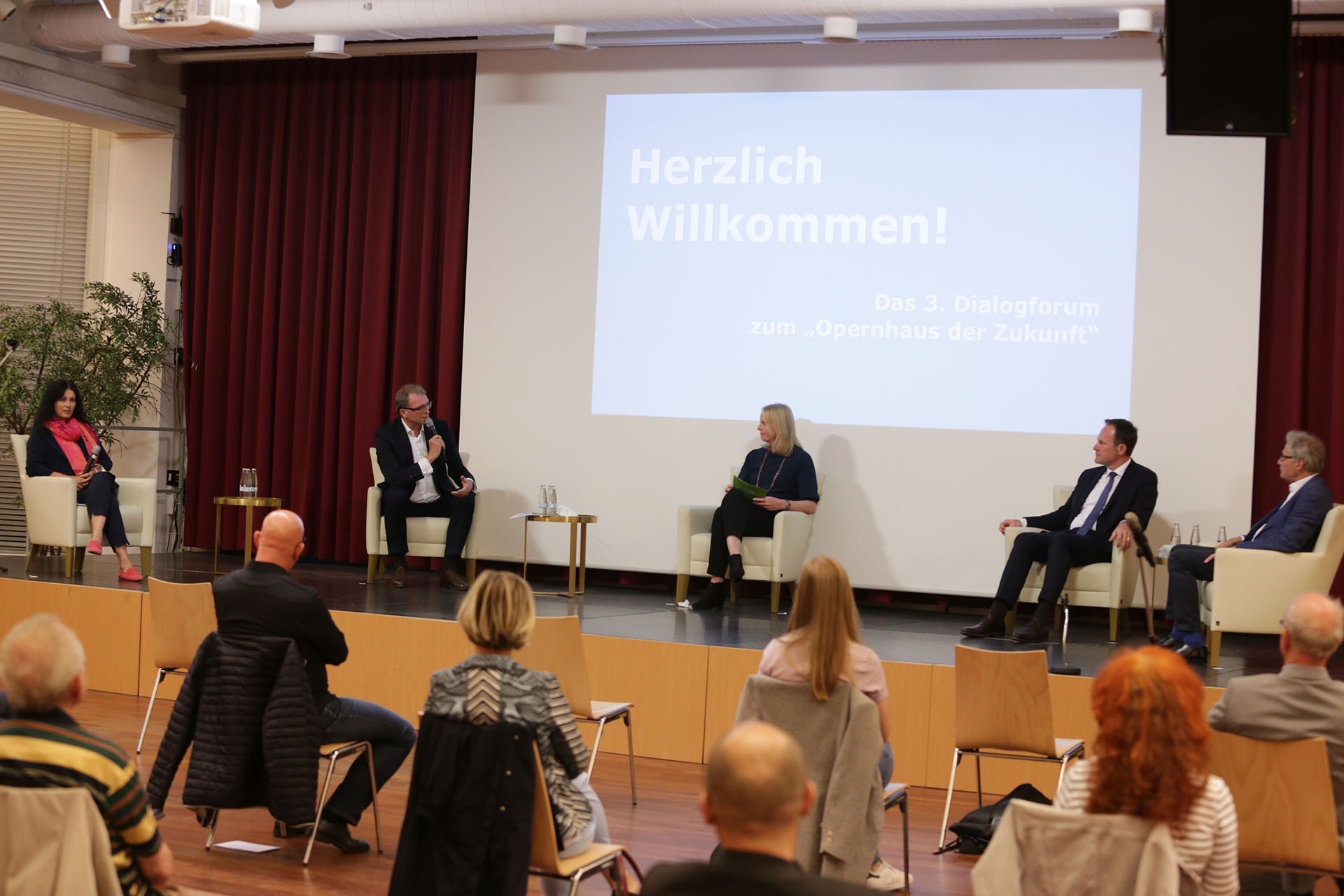 Diskussion im Dialogforum "Opernhaus der Zukunft" mit mehreren Rednern auf der B&uuml;hne und Publikum im Hintergrund.