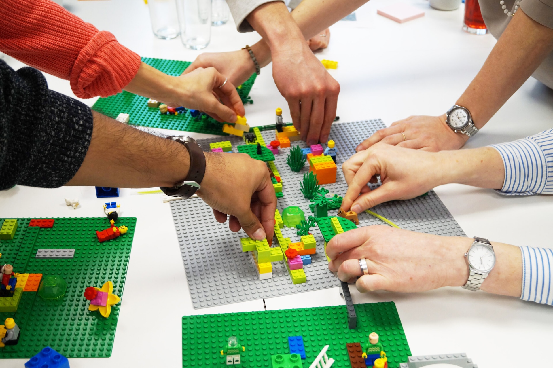 H&auml;nde von mehreren Personen bauen gemeinsam mit bunten LEGO-Steinen an einem Tisch.